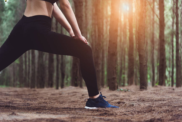 Nahaufnahme des Unterkörpers einer Frau, die Yoga macht und Beine streckt, bevor sie im Wald im Freien läuft. Sport- und Naturkonzept. Lifestyle- und Aktivitätskonzept. Thema Kiefernwälder. - Foto, Bild