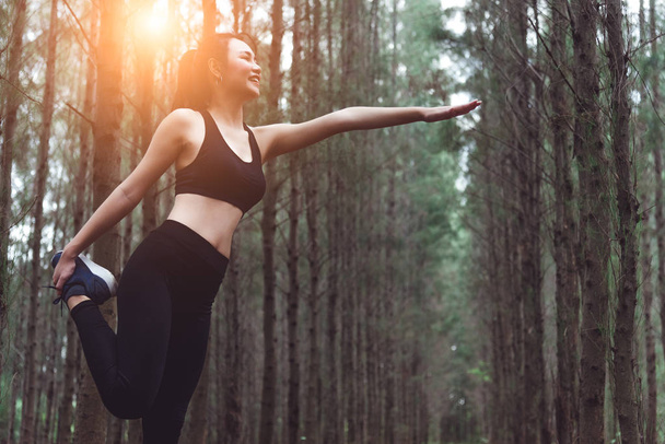 Красота азиатская женщина делает йогу и растягивая ноги перед бегом в лесу на открытом воздухе. Спорт и природа. Концепция образа жизни и деятельности. Сосновый лес
. - Фото, изображение