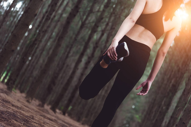 Primer plano de la parte inferior del cuerpo de la mujer haciendo yoga y estirando las piernas antes de correr en el bosque al aire libre. Concepto de deportes y naturaleza. Concepto de estilo de vida y actividad. Tema Pine woods
. - Foto, Imagen