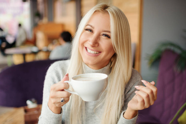Cheerful happy blond woman in cafe drinking morning coffee and smiling  - Zdjęcie, obraz