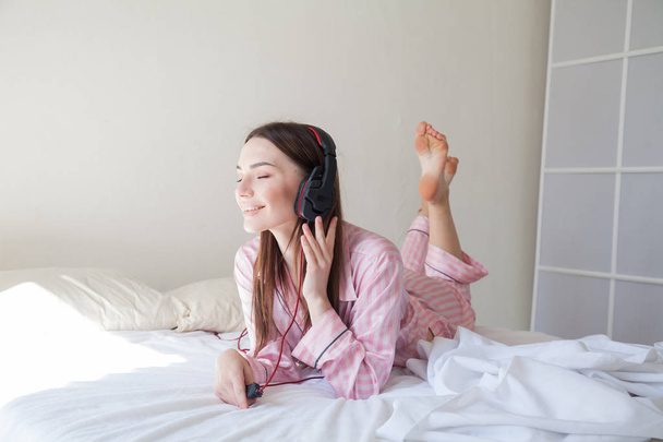 ベッド寝室でヘッドフォンで音楽を聴くパジャマで美しい女性 - 写真・画像
