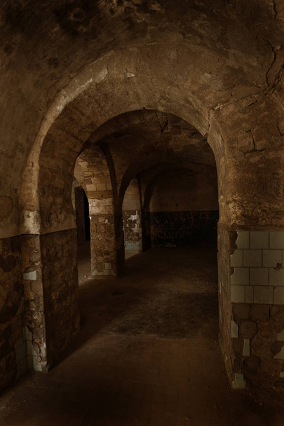 An old abandoned tunnel in an underground wine cellar. Entrance to catacombs. Dungeon Old stone fortress. As creative background for staging dark design. Mystical interior of ancient dungeon - Zdjęcie, obraz