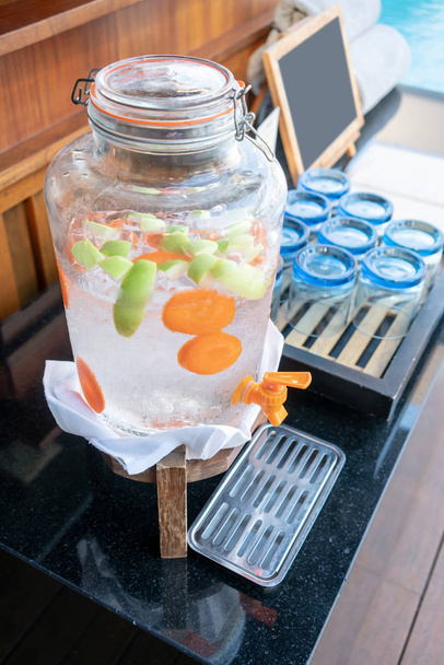 Close-up on green apple, carrot and ice in glass bottle of fruit infused water. - Photo, Image