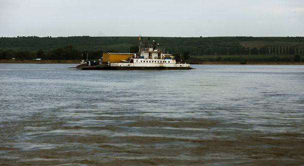 Pequenos ferries fluviais privados através do rio Danúbio transportam carros longos de carga. Um ferry de convés fluvial com vagões de carga e passageiros e passageiros no convés atravessa o Danúbio em local estreito. 2017 - Roménia
 - Foto, Imagem
