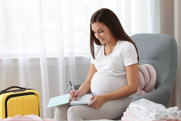 Pregnant woman writing packing list for maternity hospital at home - Foto, immagini