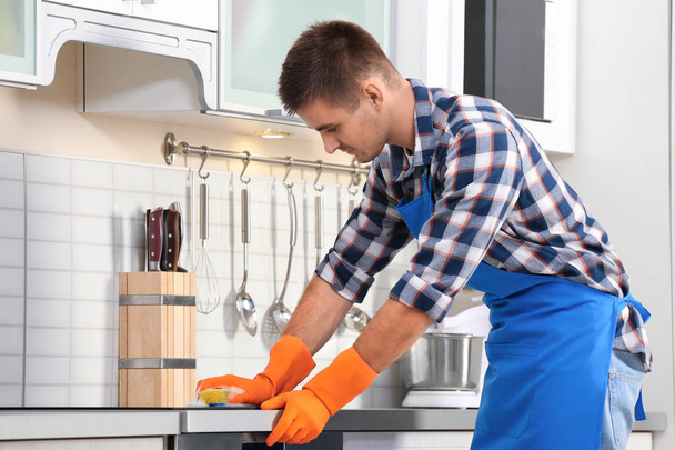 Man cleaning kitchen stove with sponge in house - Zdjęcie, obraz