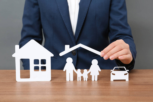 Woman with cutout paper family, house and car at table, closeup. Life insurance concept - Photo, image