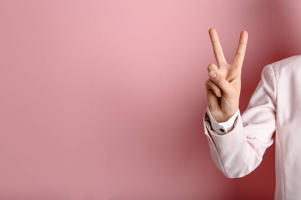 Young woman showing victory gesture on color background. Space for text - Foto, afbeelding