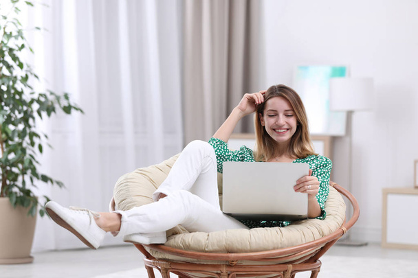 Attractive young woman with laptop in armchair at home - Fotó, kép