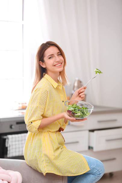 Happy young woman eating salad in kitchen. Healthy diet - Photo, image