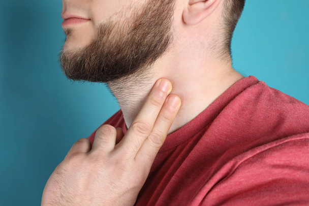 Young man checking pulse on neck against color background, closeup - Foto, Imagen