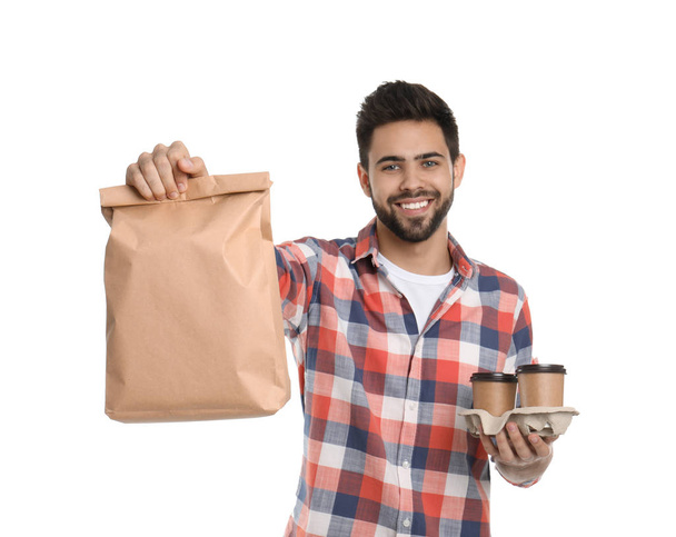 Young courier with paper bag and drinks on white background. Food delivery service - Photo, Image