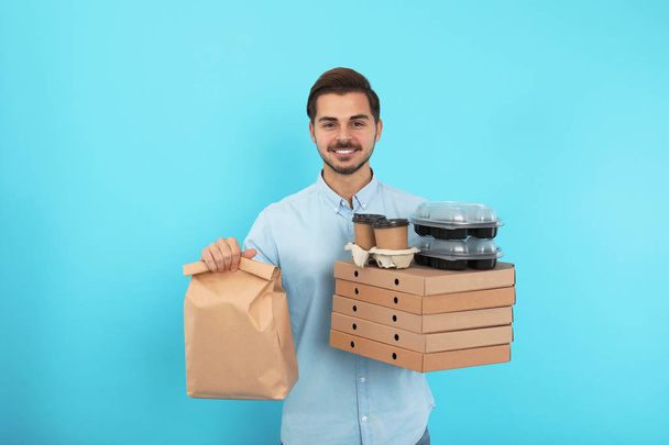 Young courier with different orders on color background. Food delivery service - Fotó, kép