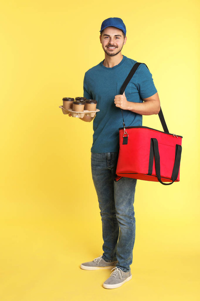 Young courier with thermo bag and drinks on color background. Food delivery service - Foto, afbeelding