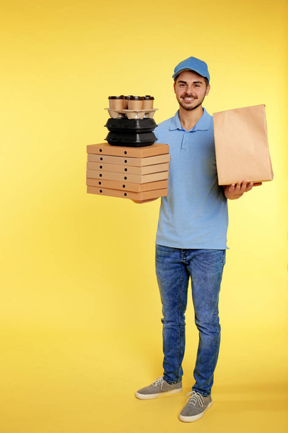 Young courier with different orders on color background. Food delivery service - Foto, afbeelding