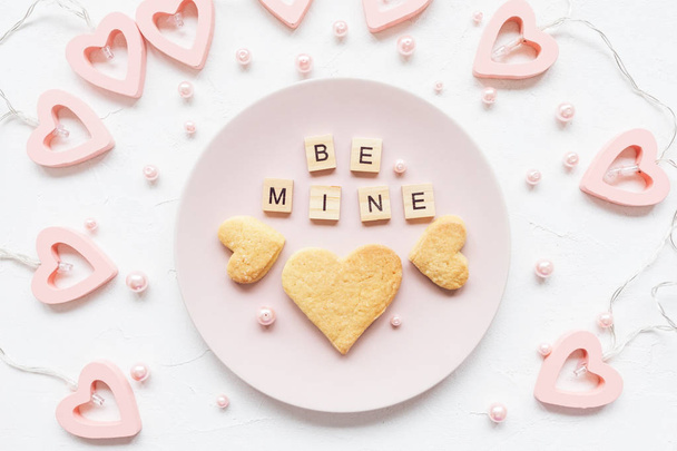 BE MINE words and heart shaped butter cookies on a pink plate and Valentine's Day decoration - heart shaped lights for a Valentines Day on a white background - Photo, Image