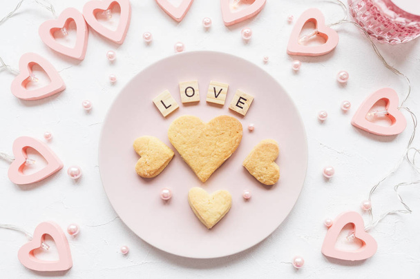 LOVE word and heart shaped butter cookies on a pink plate and Valentine's Day decoration - heart shaped lights for a Valentines Day on a white background - Фото, зображення