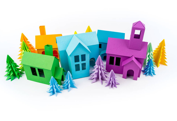 Rainbow house glued out of paper stands in the multicolored forest. White background. Children's crafts. Christmas tree. - Фото, зображення