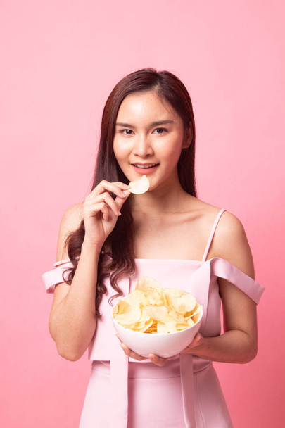 Young Asian woman eat potato chips on pink background - Valokuva, kuva