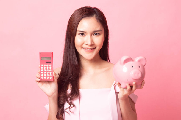 Beautiful young Asian woman with calculator and piggy bank on pink background - Zdjęcie, obraz