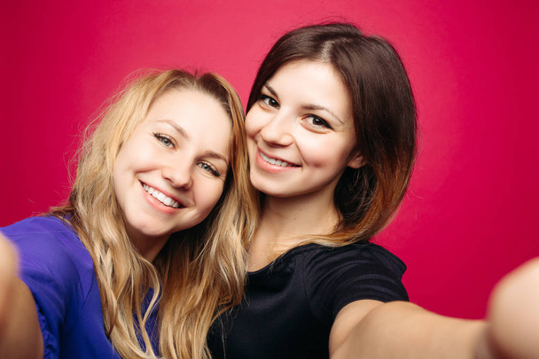 Две положительные девушки делают автопортрет улыбаясь, позируя на розовом фоне
. - Фото, изображение