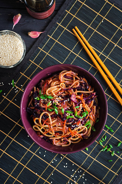 Κινέζικο φαγητό. Vegan αναδεύεται τηγανητά noodles με κόκκινο λάχανα και τα καρότα σε ένα μπολ πάνω σε μαύρο φόντο ξύλινη. Γεύμα ασιατικής κουζίνας. - Φωτογραφία, εικόνα