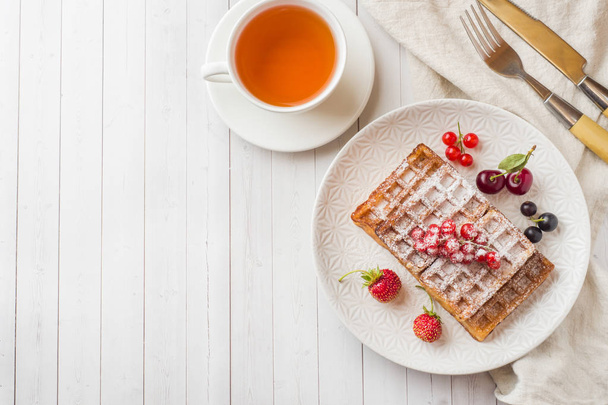 Homemade waffles with summer berries on a plate. A Cup of tea on a light table. Selective focus. - Φωτογραφία, εικόνα