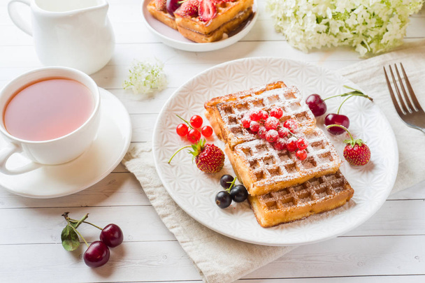 Homemade waffles with summer berries on a plate. A Cup of tea on a light table. Selective focus. - Фото, зображення