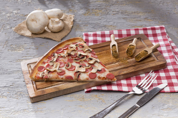 gri zemin üzerine ahşap kesme tahtası üzerinde parça İtalyan pizza ve baharat görünümü kadar kapatın - Fotoğraf, Görsel