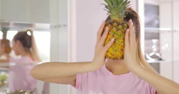 Young funny woman plays with pineapple on kitchen - Felvétel, videó