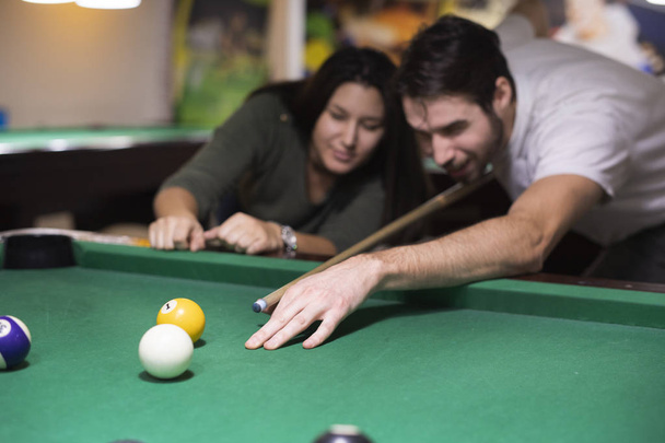 Handsome guy and a beautiful girl are playing billiards he is teaching her how to play  - Фото, изображение