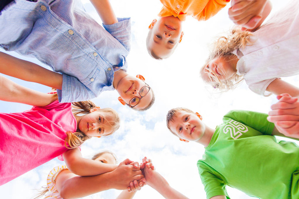 Blick von unten auf eine Gruppe glücklicher Schulkinder, die im Kreis stehen - Foto, Bild