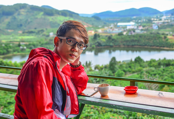 Молодой человек отдыхает в кафе с видом на горы в Далате, Центральное нагорье, Вьетнам
. - Фото, изображение