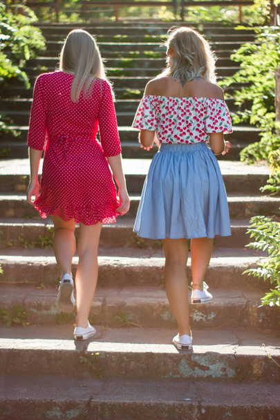 Kaksi viehättävää kaunista nuorta blondia naista puhaltaa kuplia puistossa ja ovat tyytyväisiä auringonlaskuun. Tyttöystäviä puistossa portailla
 - Valokuva, kuva