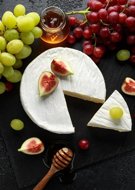 Prato de pedra de brie de queijo branco com figos, uva verde e vermelha e mel
. - Foto, Imagem