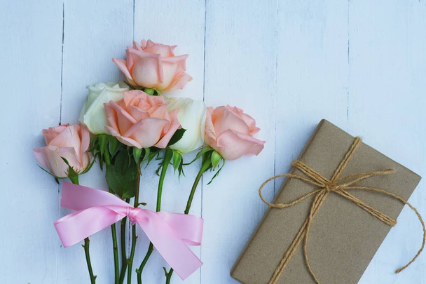Lovely soft orange pink color rose tied by pink ribbon and brown gift box on white wood table background, sweet valentine present concept, copy space - Foto, Bild
