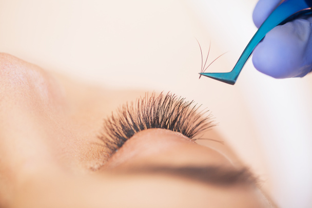 Eyelashes extensions. Fake Eyelashes. Eyelash Extension Procedure. Professional stylist lengthening female lashes. Master and a client in a beauty salon - Photo, Image