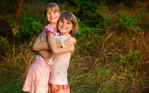 Две очаровательные маленькие сестры смеются и обнимаются в солнечный день в летнем парке
 - Фото, изображение