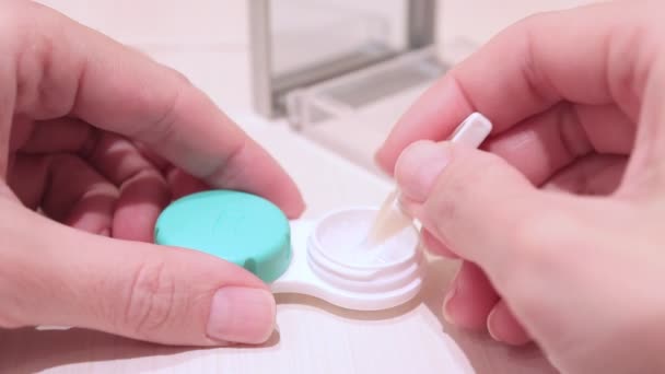Cropped female hands taking contact lenses out of a container using tweezers - Filmati, video