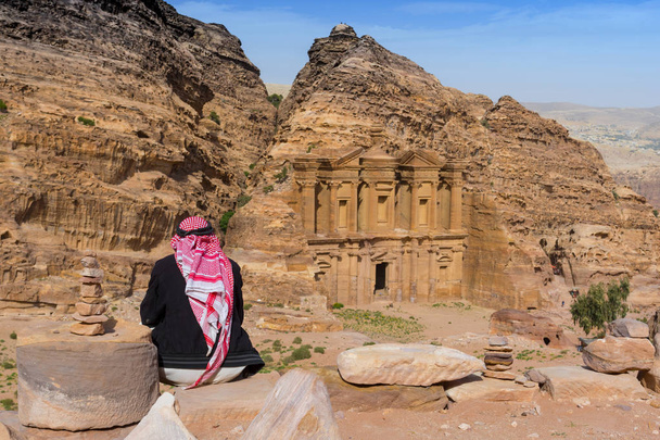 Beduíno olhando para o túmulo de pedra esculpida ornamentado conhecido como O Mosteiro El Deir Nabataean cidade antiga Petra Jordan
. - Foto, Imagem