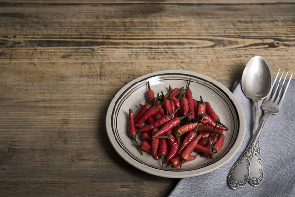 Red chili pepper on a vintage plate, antique silver spoon and fork, dried chillies on wooden background. Top view. Copy spase. - Foto, Imagem