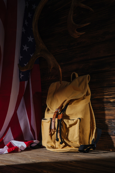 σακίδιο, κέρατα και αμερικανική σημαία σε ξύλινη επιφάνεια, έννοια του ταξιδιού  - Φωτογραφία, εικόνα
