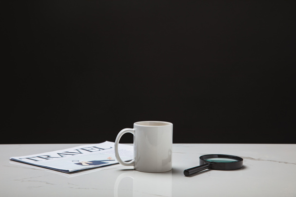 close-up view of cup, magnifying glass and travel newspaper on white surface on black - Photo, Image