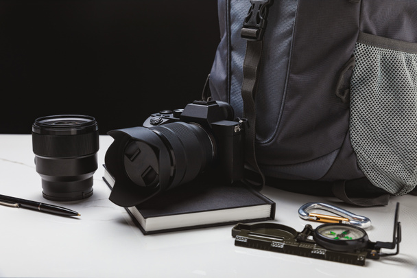 close up view of photo camera with lens, pen, notebook, compass and backpack on black - Foto, afbeelding