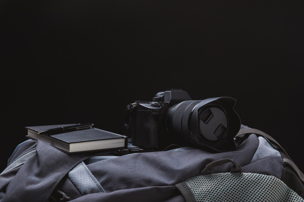 Detailní pohled fotoaparátu s Poznámkový blok a pero na batoh izolované na černém pozadí - Fotografie, Obrázek