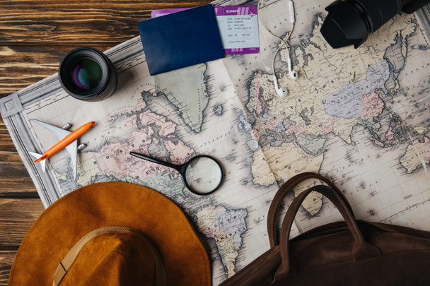 kahverengi deri çanta, şapka, Büyüteç Camı, küçük maket uçak, earphones, fotoğraf makinesi, objektif ve pasaport ve biniş kartı harita üzerinde en iyi görünümü  - Fotoğraf, Görsel