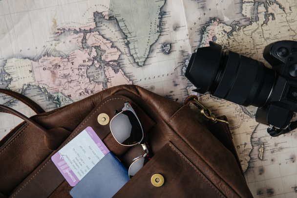 vista superior de la bolsa de cuero con pasaporte, billete, gafas de sol, cámara y mapa
 - Foto, Imagen