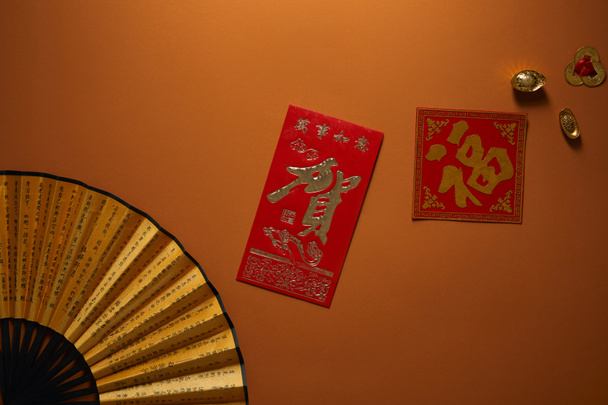 top view of fan with hieroglyphs and golden decorations on brown background, chinese new year composition - Photo, Image
