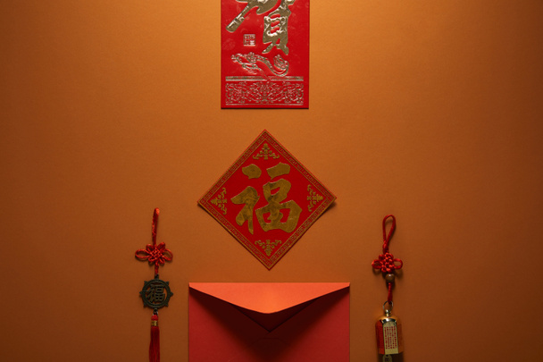 roter Umschlag, Hieroglyphen und traditionelle Dekorationen auf braunem Hintergrund, chinesisches Neujahrskonzept - Foto, Bild