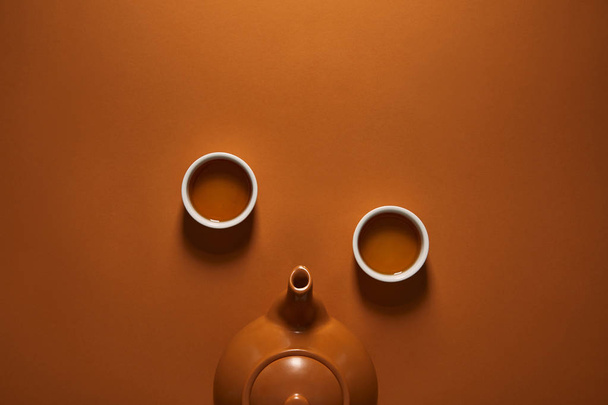 ylhäältä näkymä ruskea keraaminen kiinalainen teekannu ja kupit teetä ruskealla pohjalla
   - Valokuva, kuva